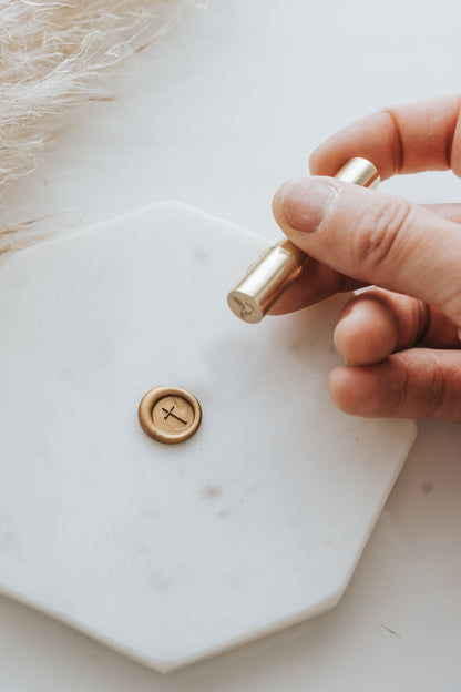 A simple cross mini brass wax seal stamp pressing a cross design into gold sealing wax 