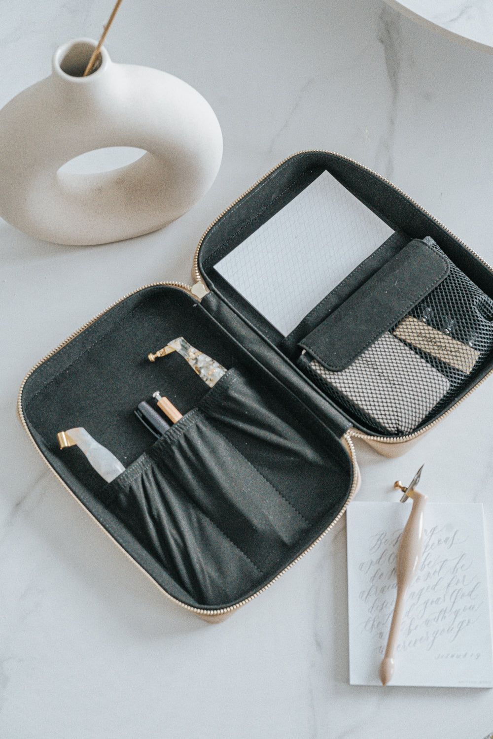 A calligraphy travel kit filled with calligraphy supplies on a white marble table next to a ceramic vase