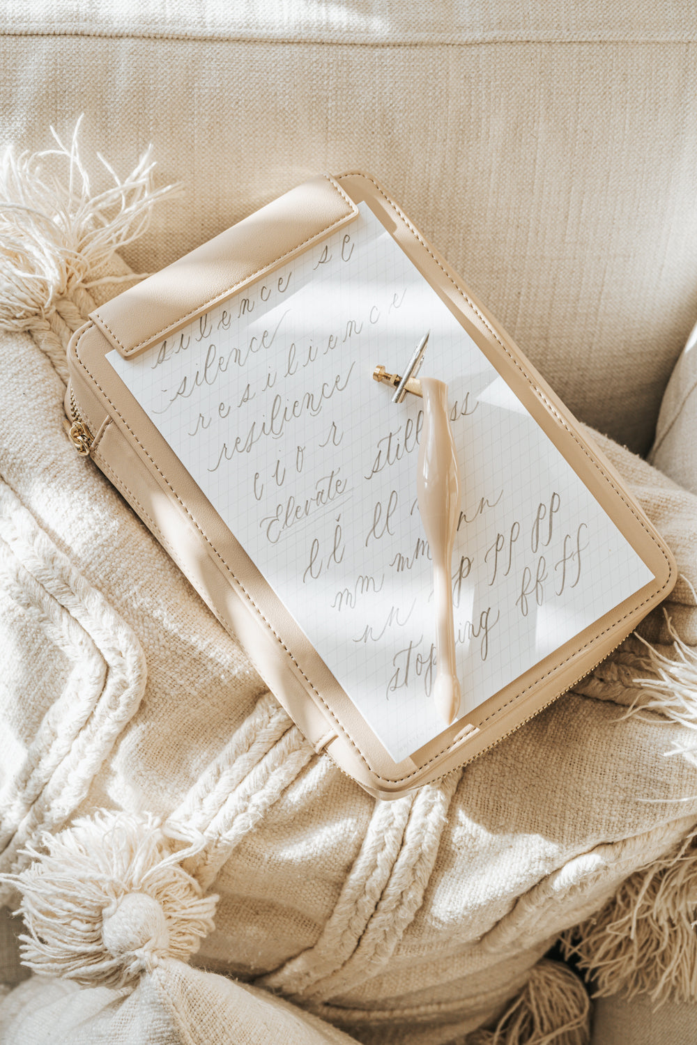 Beige Calligraphy Travel Kit with a practice sheet and blush oblique pen, resting on a textured neutral cushion.