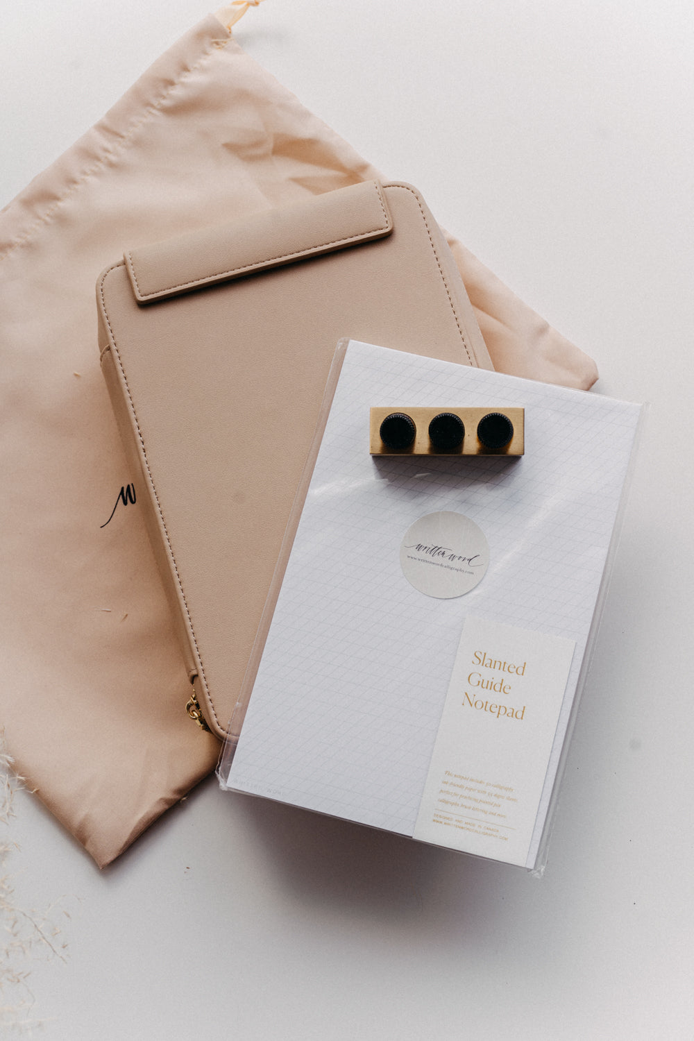 A beige travel kit on a beige dust bag with a slanted guide notepad and mini tilted inkwell on a white surface