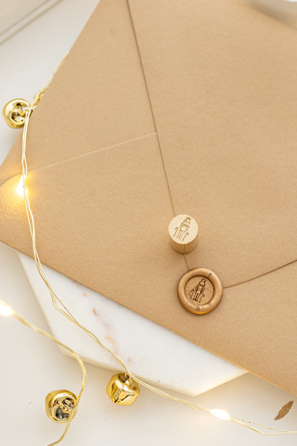 Elegant holiday mini wax seal stamp with nutcracker design in gold wax on a kraft envelope, part of Written Word Calligraphy’s Holiday Collection.