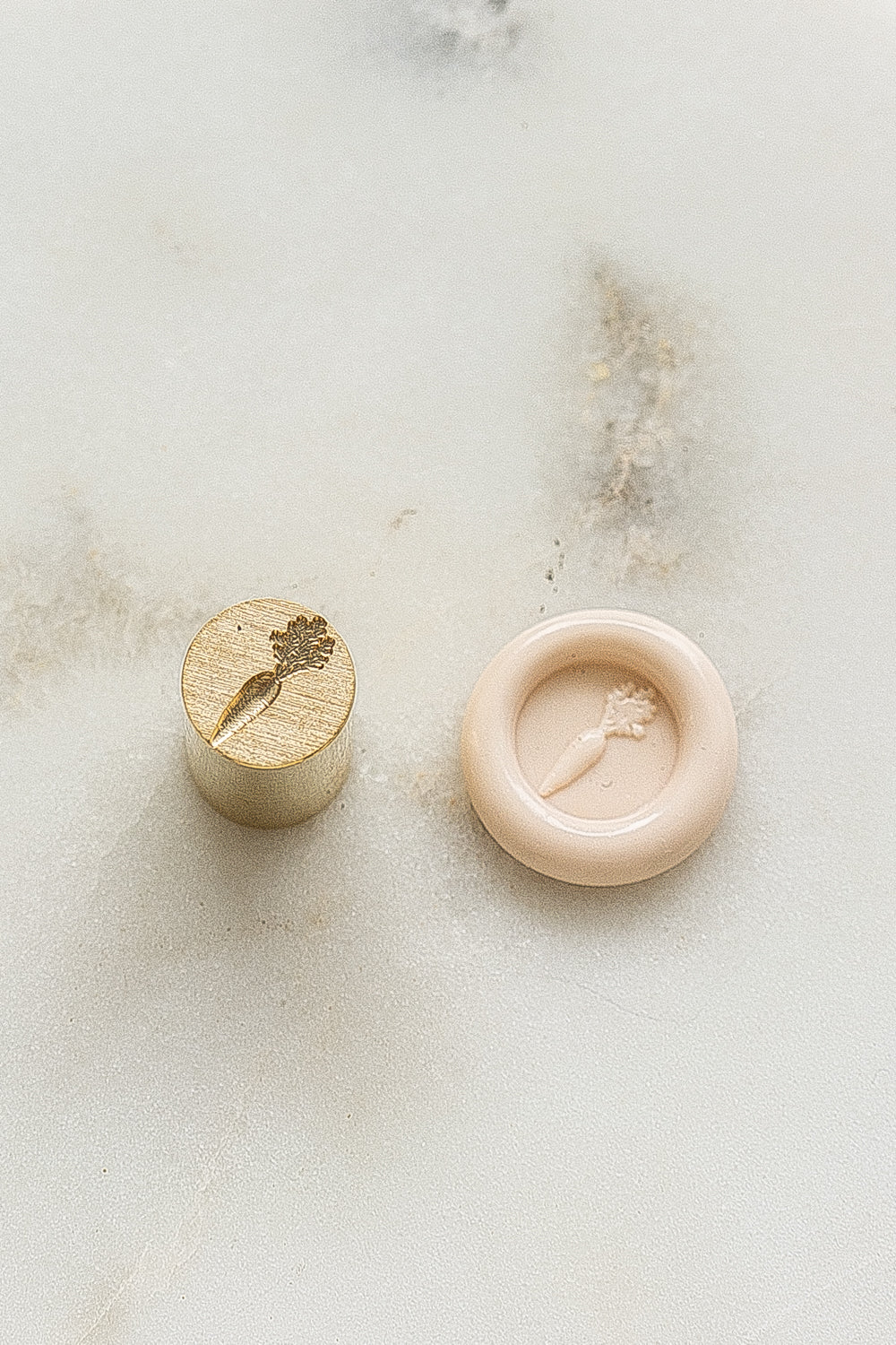 A mini brass wax seal stamp head with a 3D carrot design beside a blush wax seal impression on a white marble surface