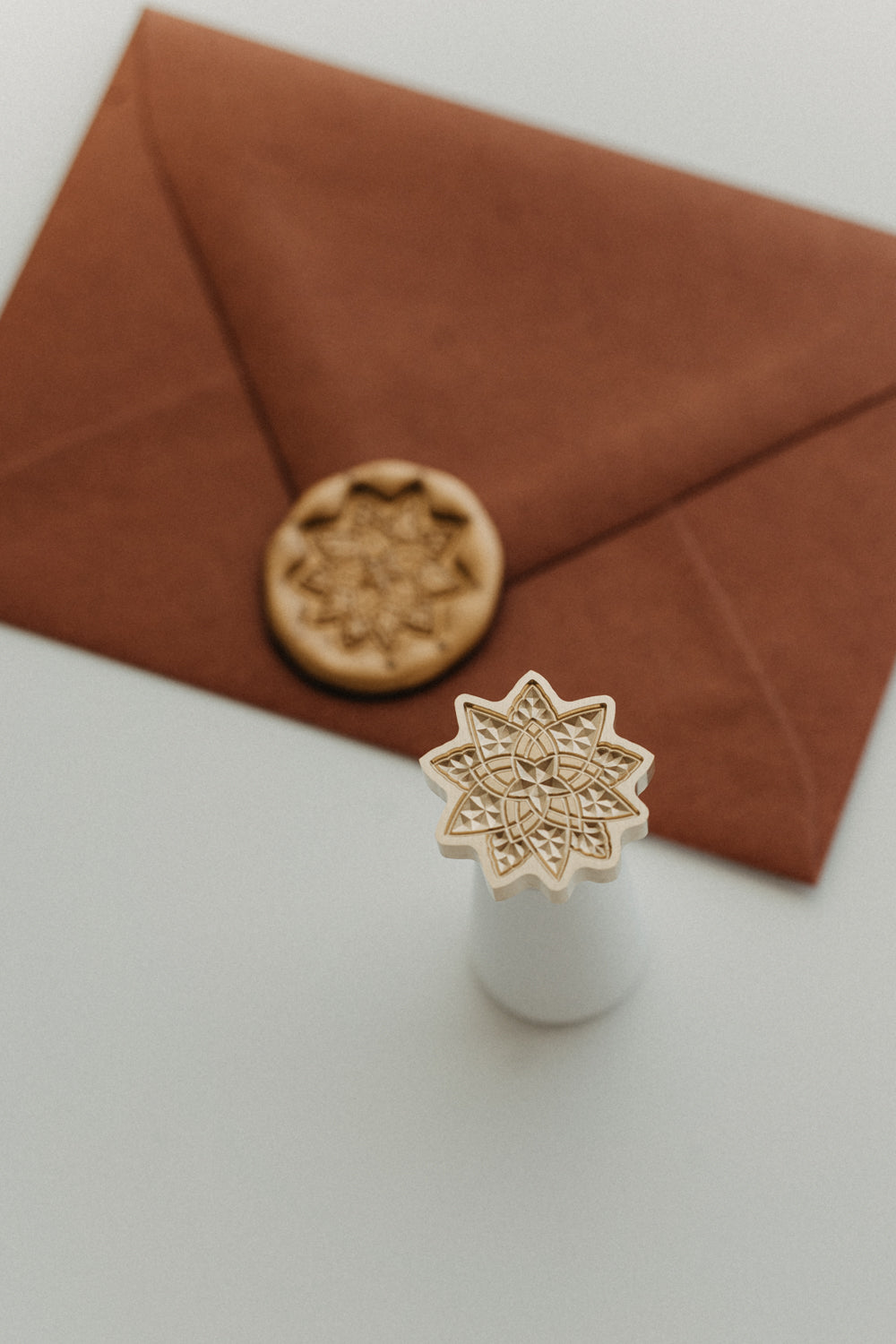 Close-up of a geometric star brass wax seal stamp with a gold wax-sealed warm brown envelope in the background.