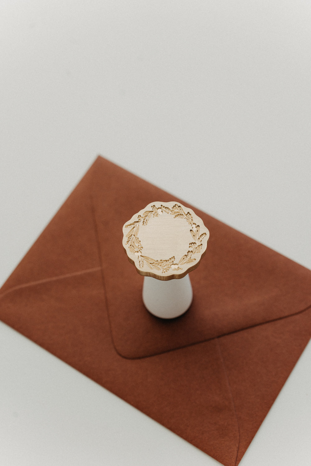 White-handled brass wax seal stamp with an engraved celestial star design on a warm brown envelope.