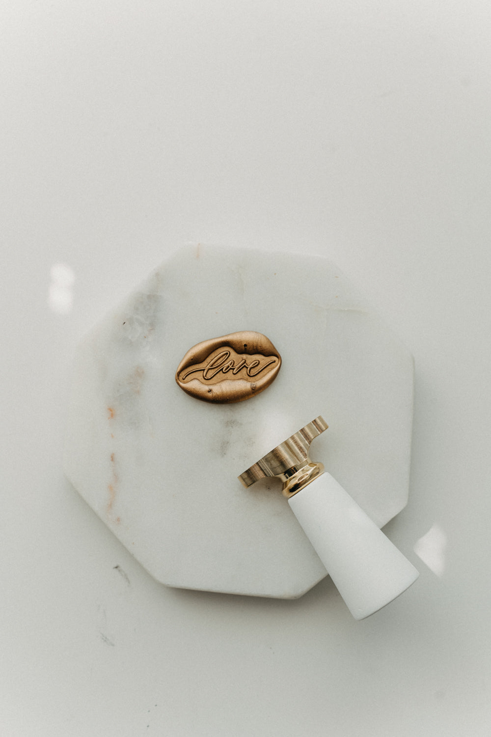 Gold “love” wax seal and white-handled brass wax seal stamp on a white marble coaster.