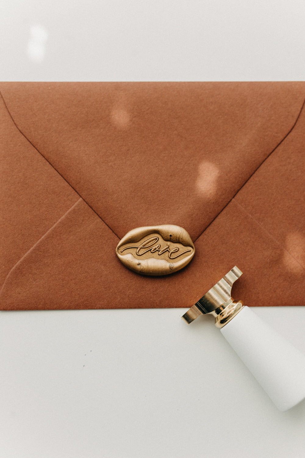 Close-up of a gold “love” wax seal securing a warm brown envelope with a white-handled brass stamp.