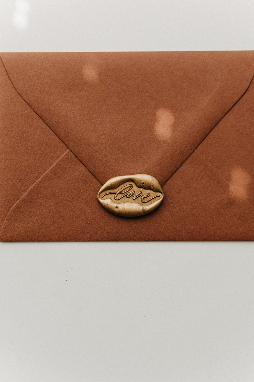 Gold “love” wax seal centered on the flap of a warm brown envelope.
