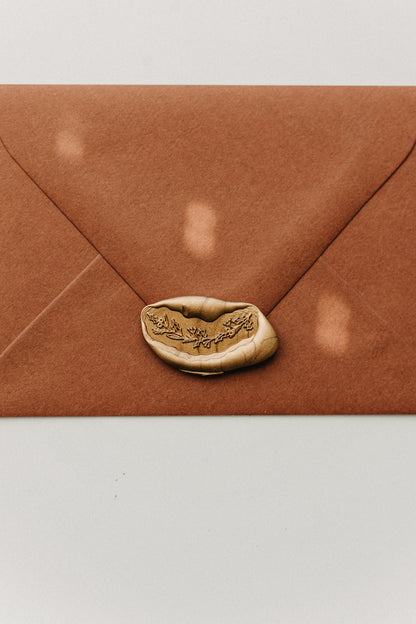 Metallic gold botanical garland wax seal securing a warm brown envelope.