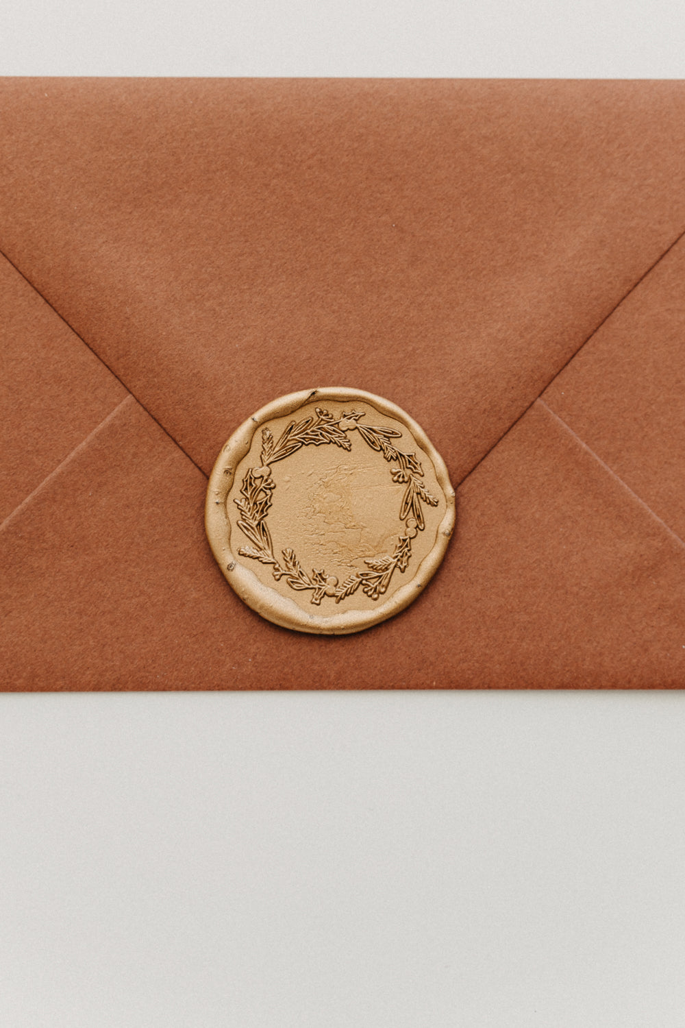 Close-up of a gold botanical wreath wax seal securing the flap of a warm brown envelope.