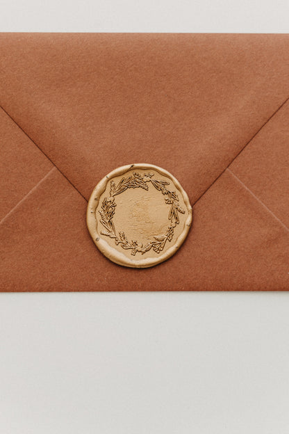 Close-up of a gold botanical wreath wax seal securing the flap of a warm brown envelope.