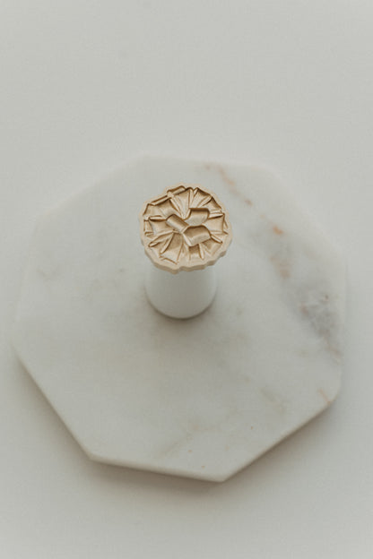 Gift bow wax seal stamp with brass design and white wooden handle on octagonal marble tray