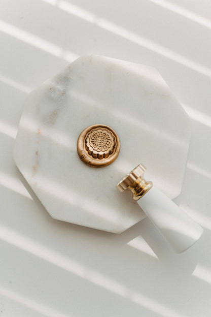 Gold mooncake wax seal stamp with floral brass head on white marble tray for Mid-Autumn Festival