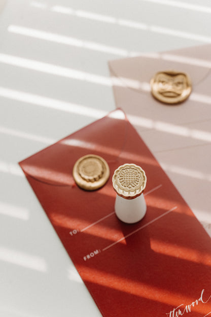 Mooncake wax seal stamp with gold wax seals on red Mid-Autumn Festival gift envelopes, floral brass design