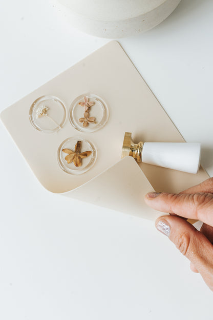 Clear wax seals with pressed flowers on beige silicone mat with wax seal stamp and hand lifting mat
