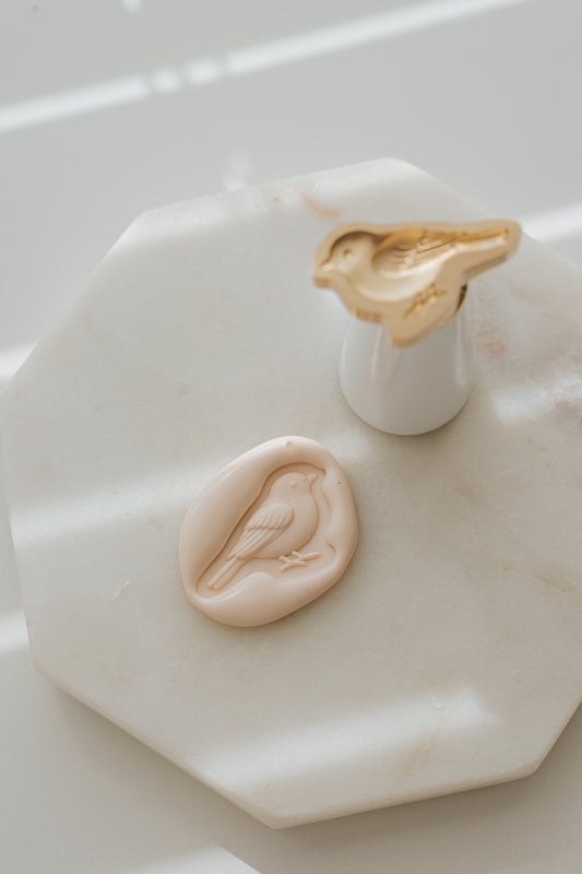 Sakura songbird wax seal with brass stamp on marble surface