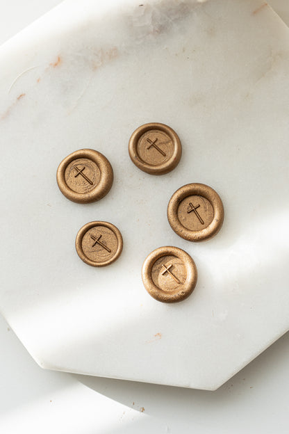 Close-up of gold sealing wax stamps with a cross design made using a mini wax seal stamp on a marble background.
