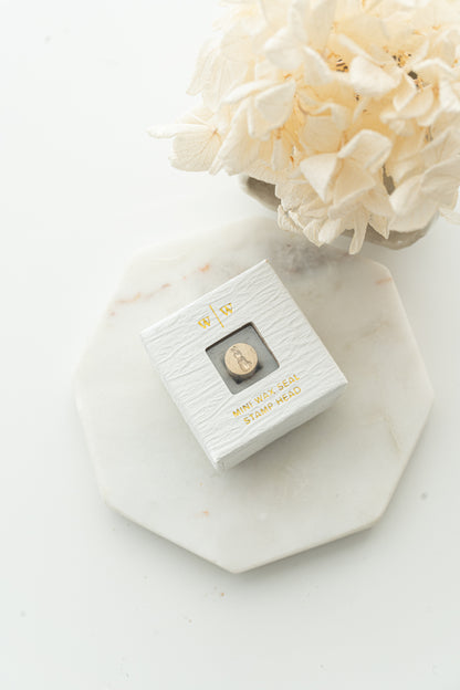 Mini wax seal stamp head in white textured box with gold foil text, styled with dried flowers on marble tray