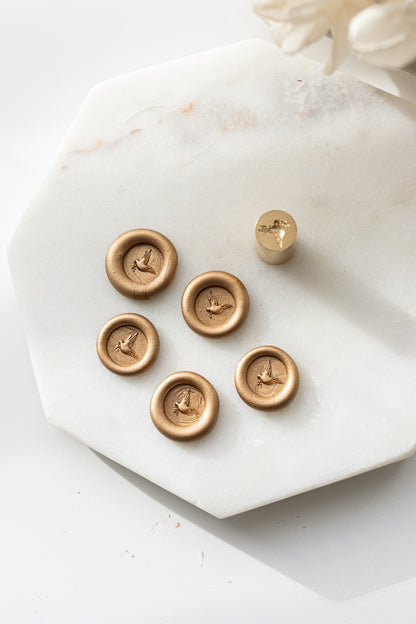 Set of five gold wax seals with dove design and matching mini stamp head on marble background