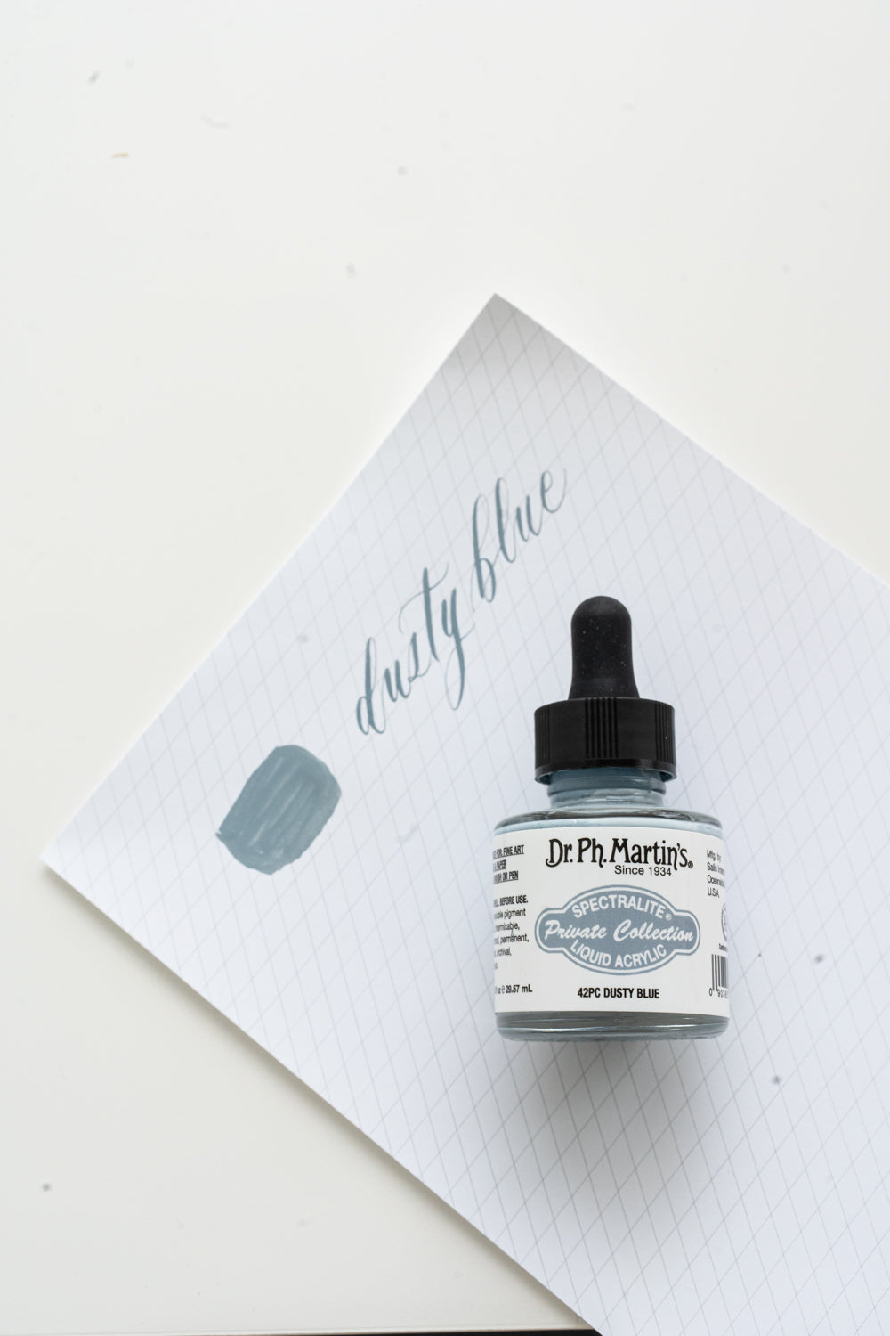 Dusty blue calligraphy ink bottle with hand lettering sample on grid paper for modern calligraphy