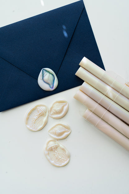 Navy envelope with an iridescent shell wax seal beside Mother-of-Pearl sealing wax sticks and ocean-inspired jellyfish and seashell wax seals.