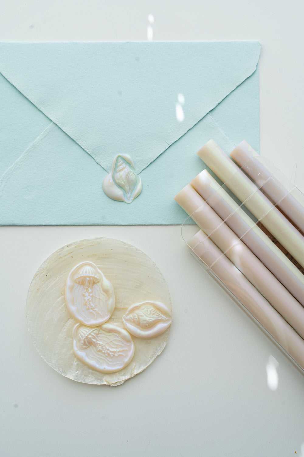 Mother-of-pearl sealing wax sticks beside a pale blue envelope and ocean-inspired wax seals with jellyfish and seashell designs.