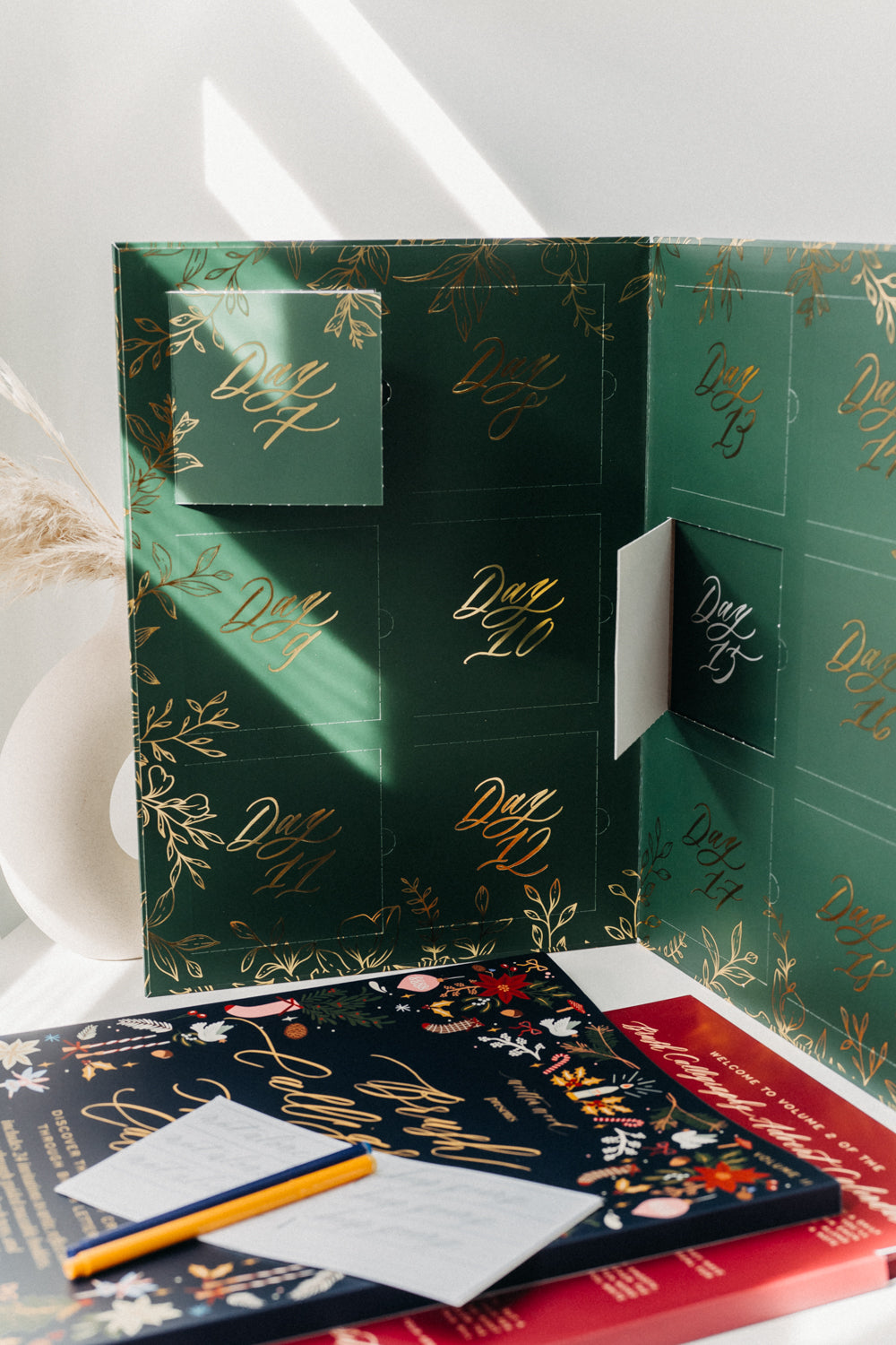 Open green Brush Calligraphy Advent Calendar with numbered daily doors, practice booklets and yellow brush pen.
