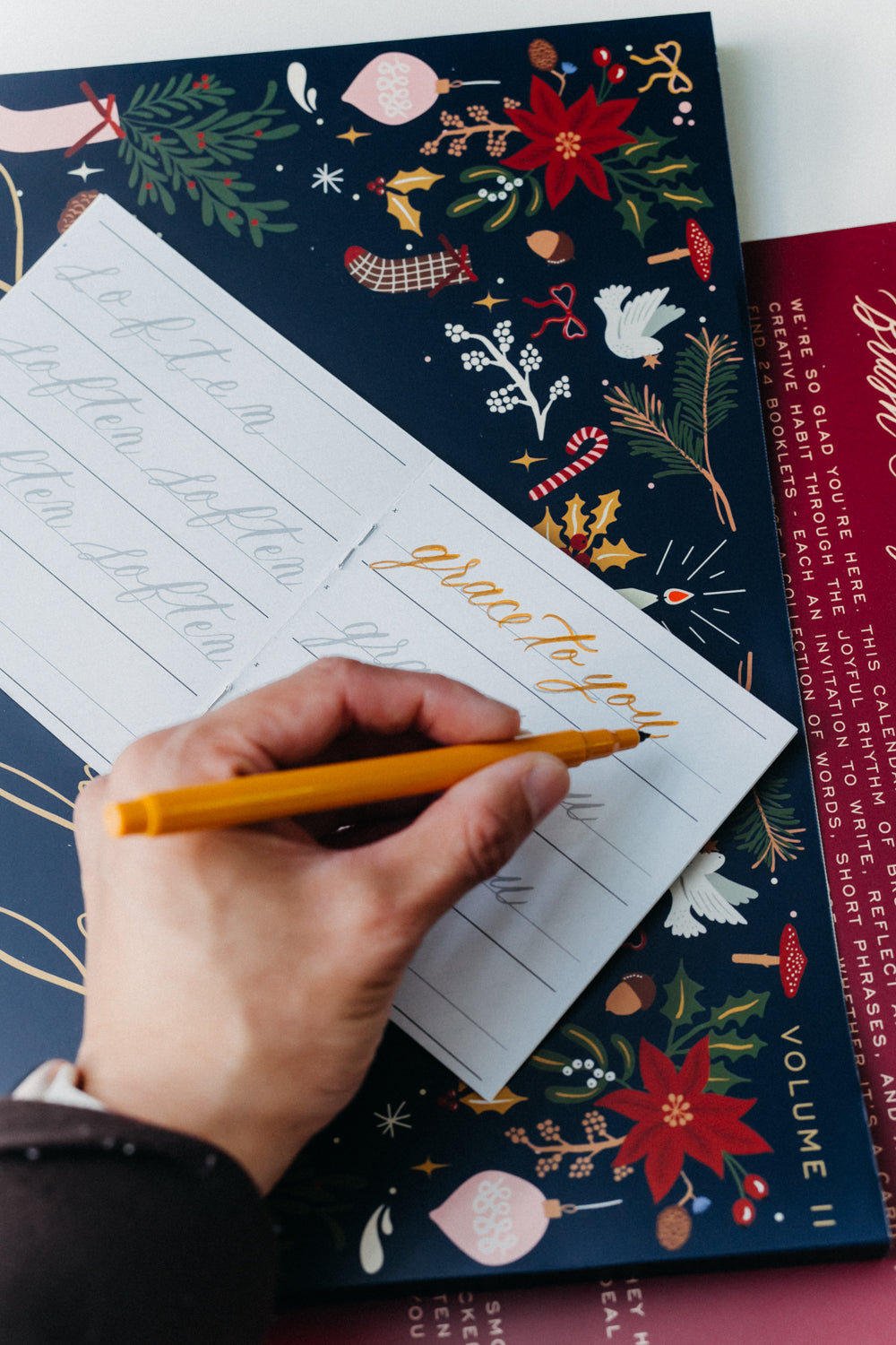 Hand practicing “grace to you” calligraphy in an Advent Calendar Volume II holiday lettering workbook.
