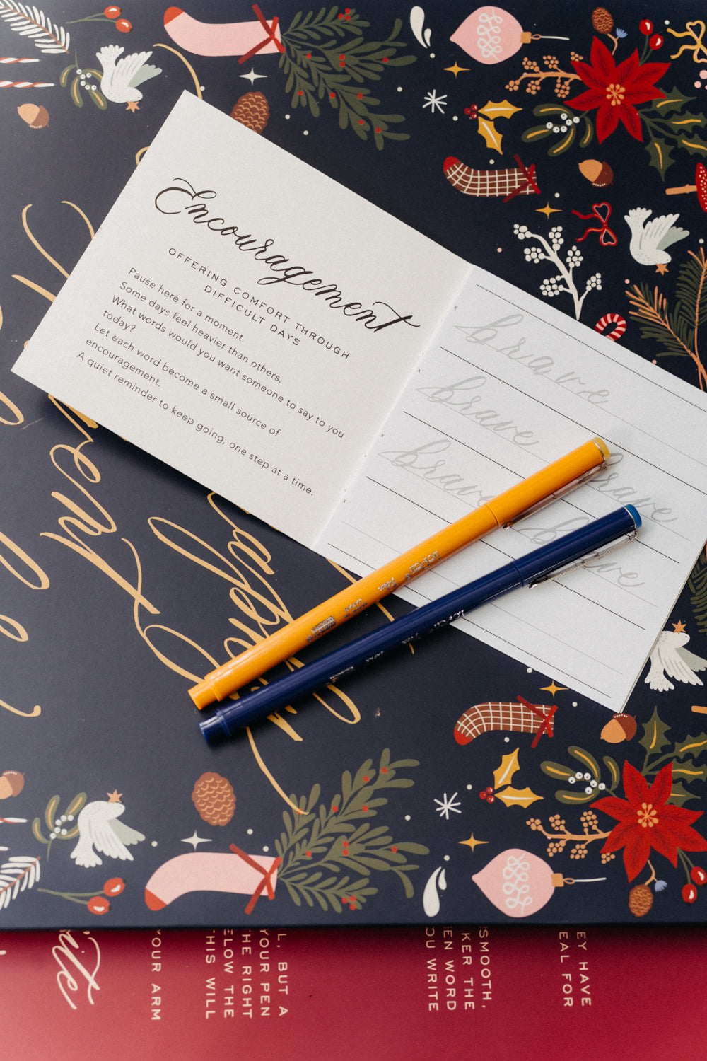 Encouragement calligraphy booklet, practice sheet and colorful pens on a festive Christmas Advent calendar.