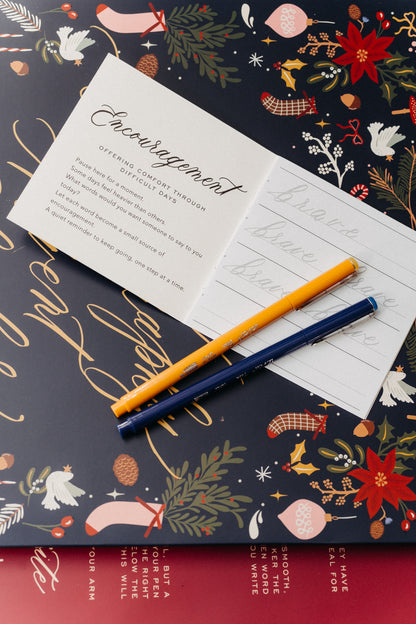 Encouragement calligraphy booklet, practice sheet and colorful pens on a festive Christmas Advent calendar.