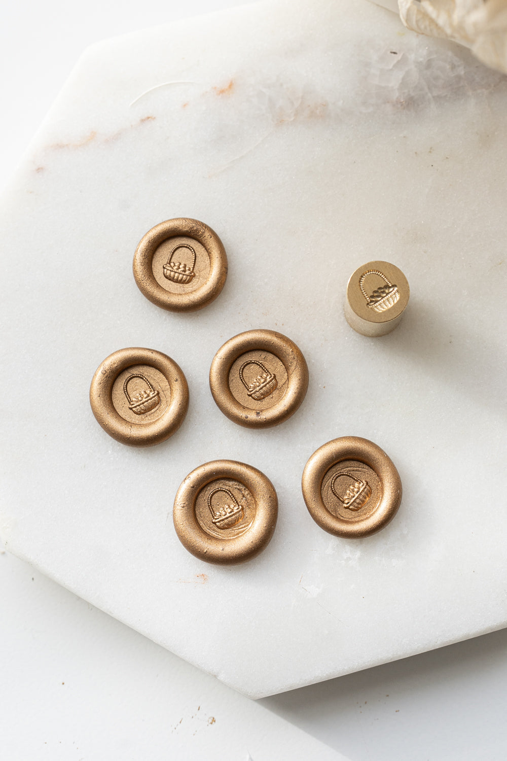 Close-up of gold sealing wax stamps with a 3d illustration of a basket of eggs made using a mini wax seal stamp on a marble background.