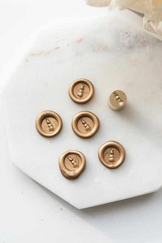 Set of five gold wax seals with bunny design and matching mini stamp head on marble background
