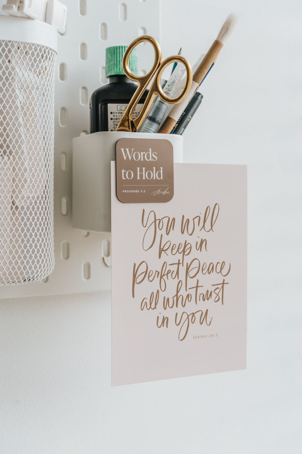 Calligraphy scripture print clipped to wall organizer with stationery tools, Proverbs 3:3 card styling