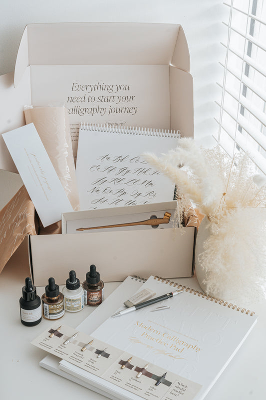 Beginner calligraphy supplies including ink, nibs, pen holder, and alphabet practice sheets