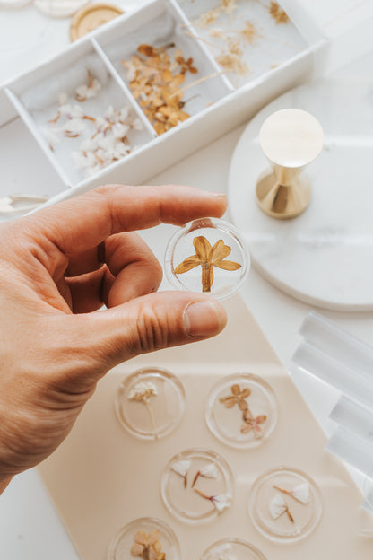 Hand holding clear wax seal with pressed flower, surrounded by floral wax seals and wax sealing tools