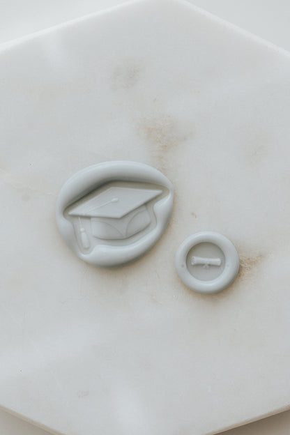 Pale gray graduation wax seal with cap and diploma design on marble background