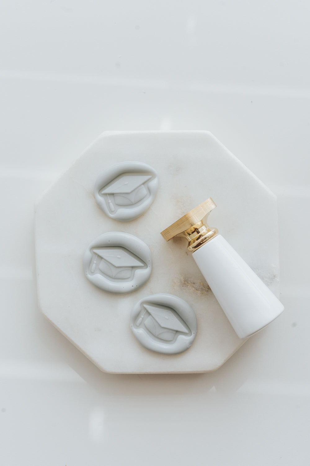 Graduation cap wax seal stamps and pale gray wax seals on marble
