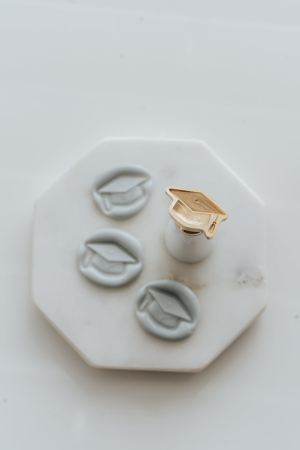 Graduation cap wax seal stamp with white handle and pale gray wax seals