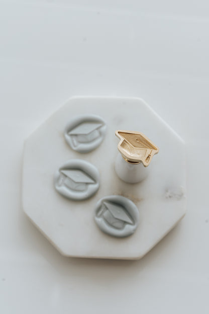 Graduation cap wax seal stamp with white handle and pale gray wax seals