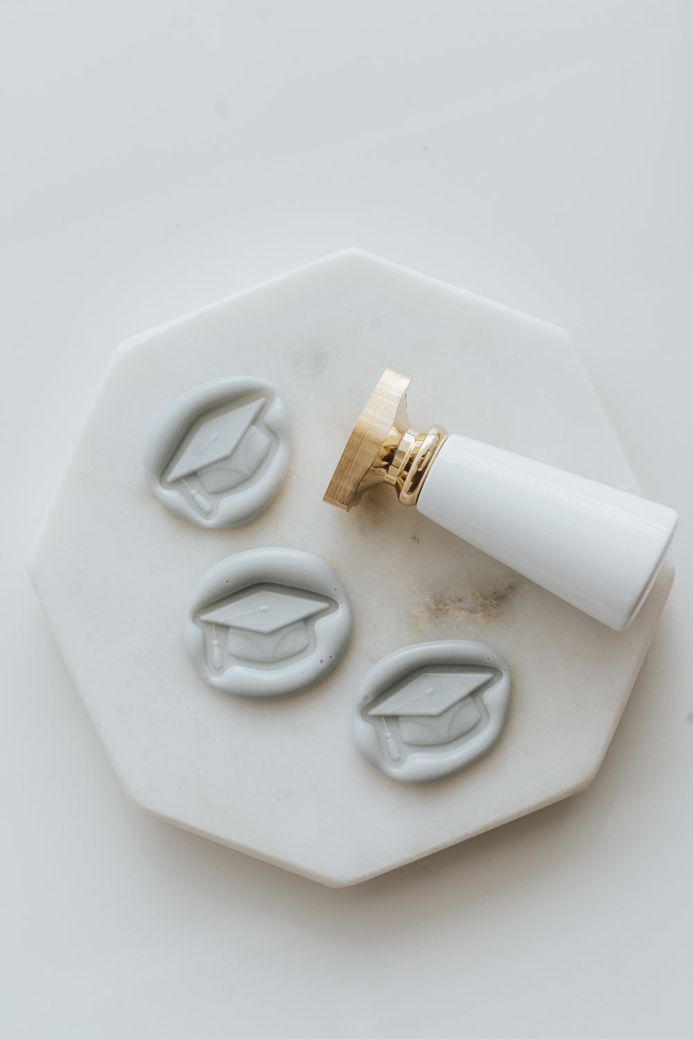 Pale gray graduation cap wax seals with brass wax seal stamp on marble