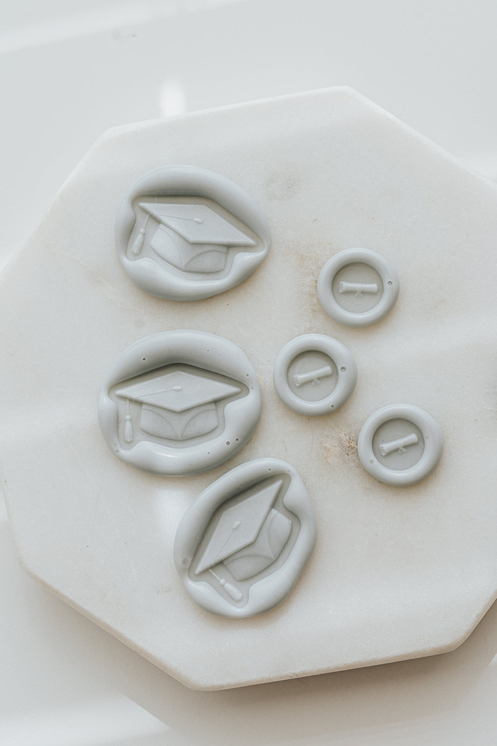 Pale gray graduation caps wax seals and diploma mini wax seals on marble surface