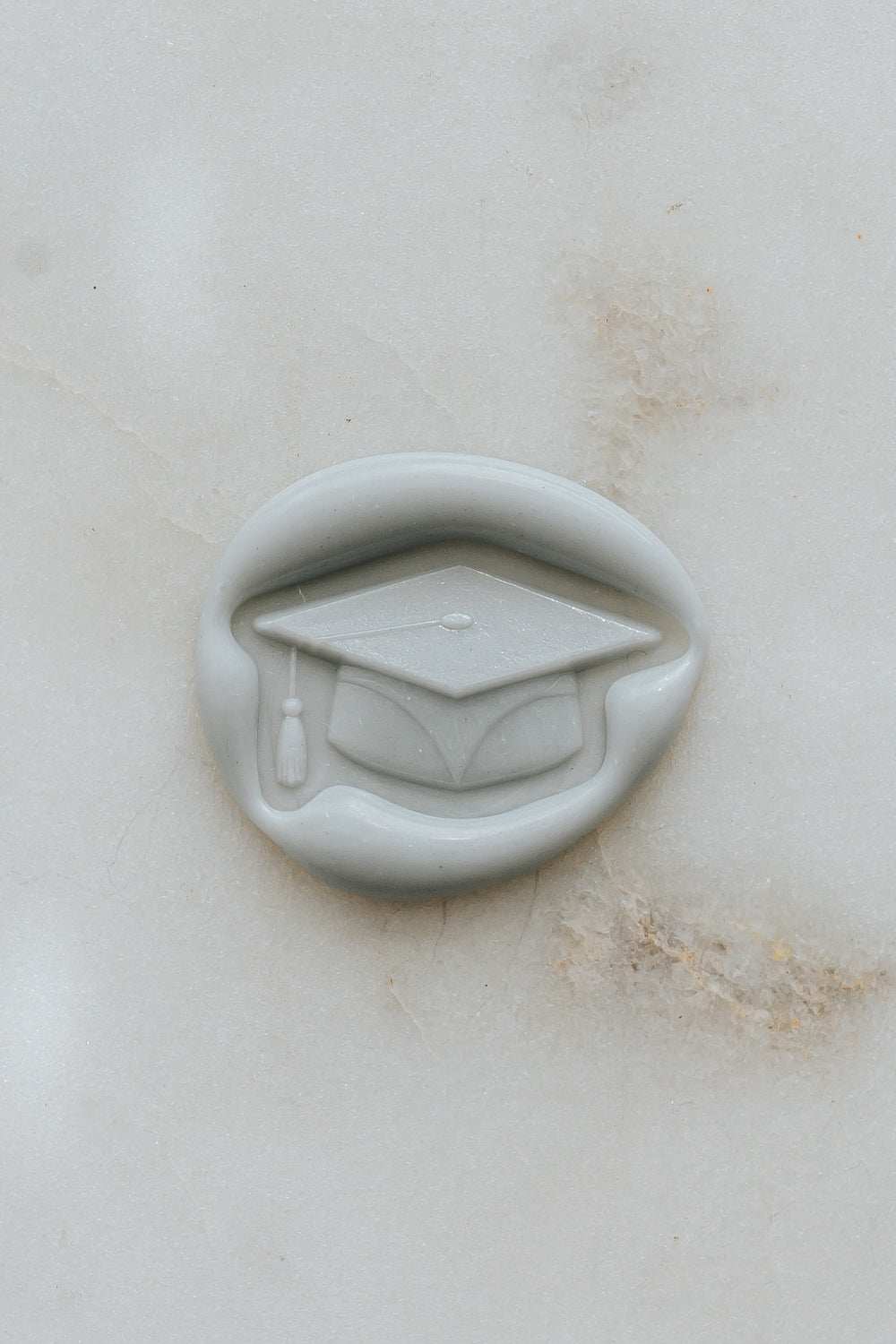 Pale gray graduation wax seal with cap design on marble background