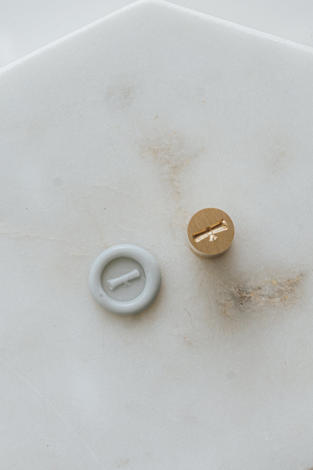 Pale gray diploma wax seal with mini wax seal stamp head on marble background