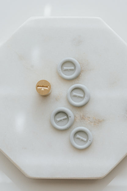 Pale gray mini wax seals with diploma design and brass stamp head on marble surface