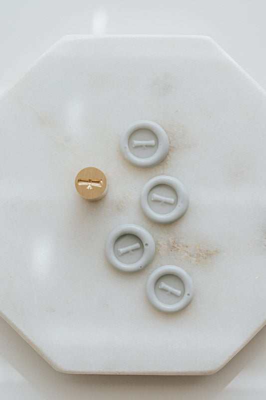 Pale gray mini wax seals with diploma design and brass stamp head on marble surface