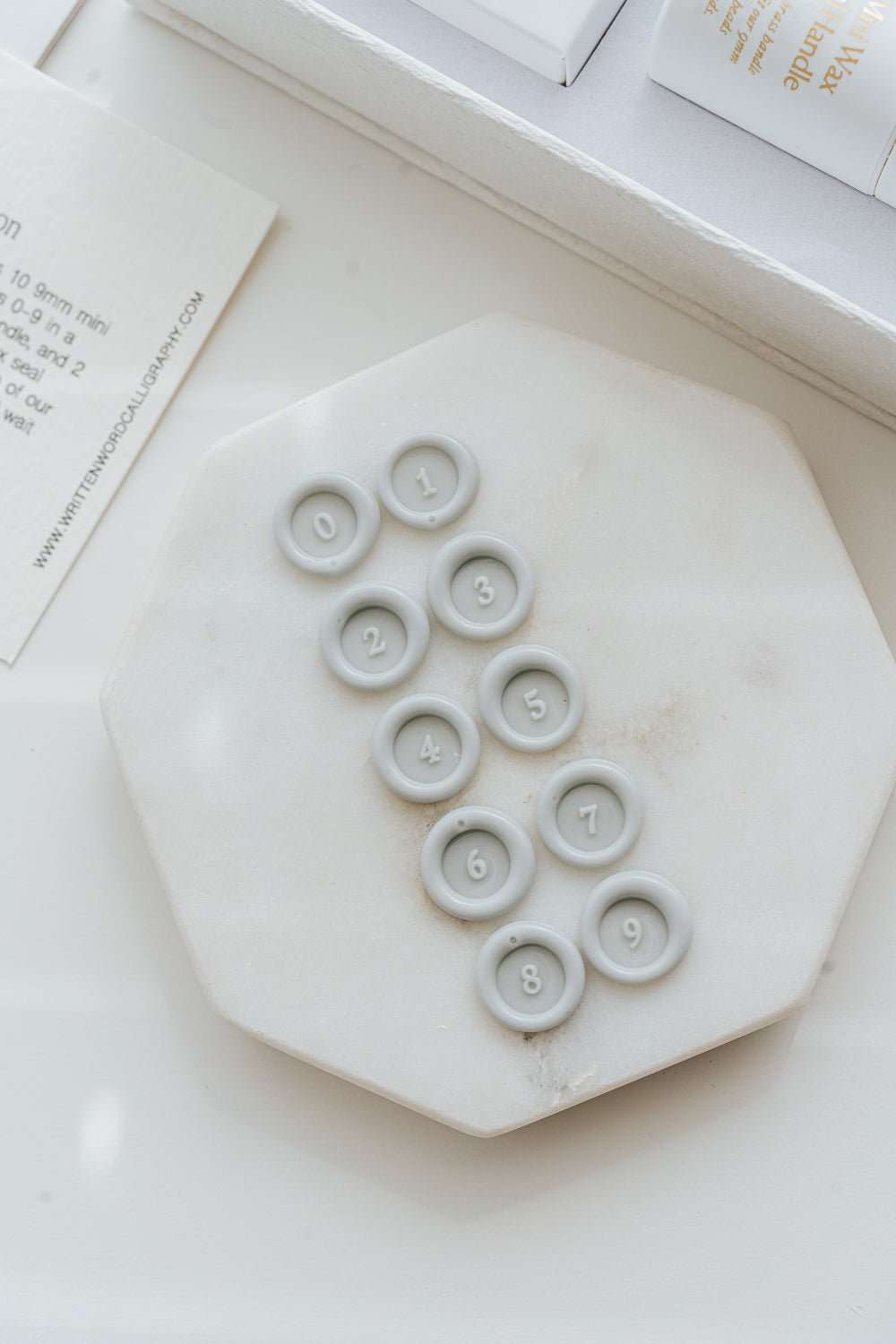 Pale gray wax number seals 0 to 9 displayed on marble 