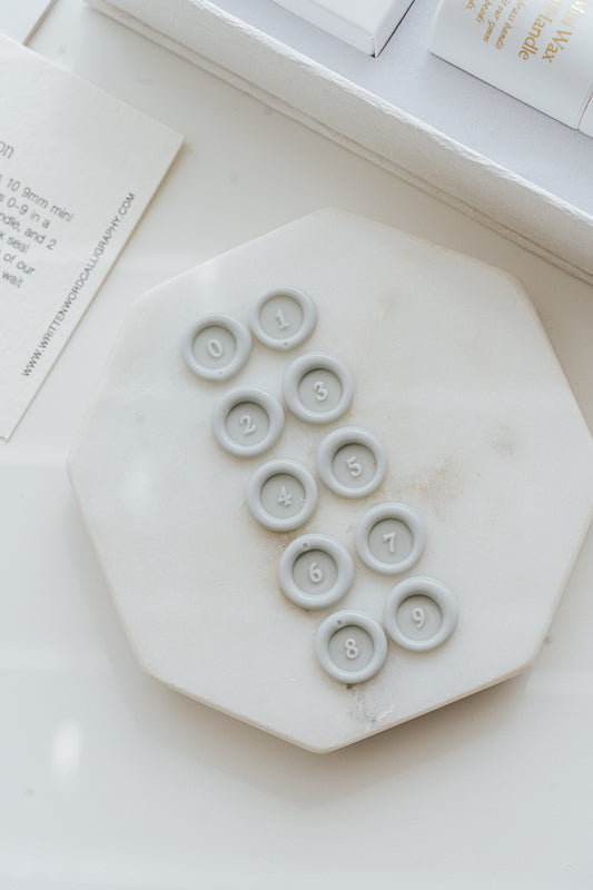 Pale gray wax number seals 0 to 9 displayed on marble 