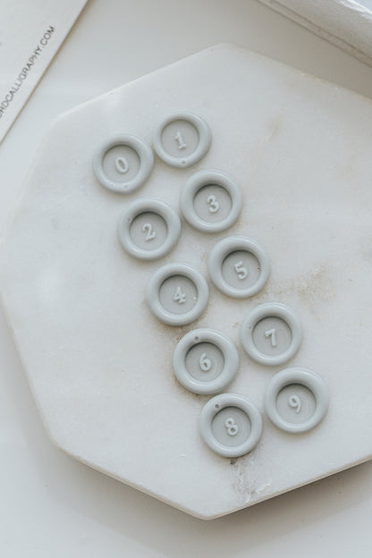 Mini wax seal numbers 0 to 9 impressions in white wax arranged on marble tile