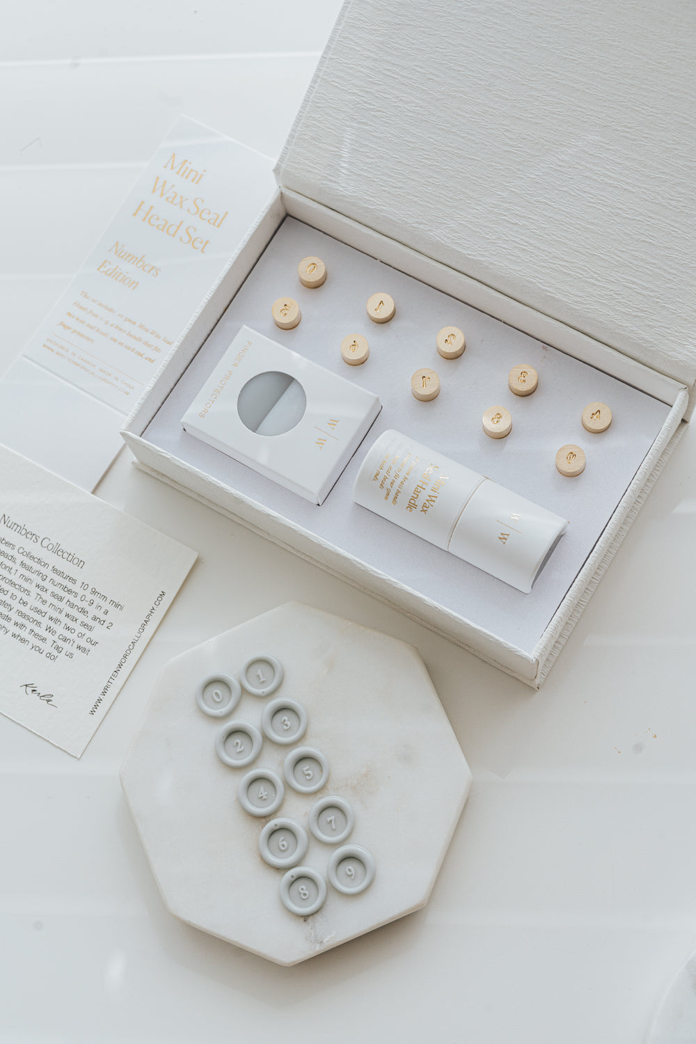 Mini wax seal number set with box, handle, and sample wax seals arranged on marble tile