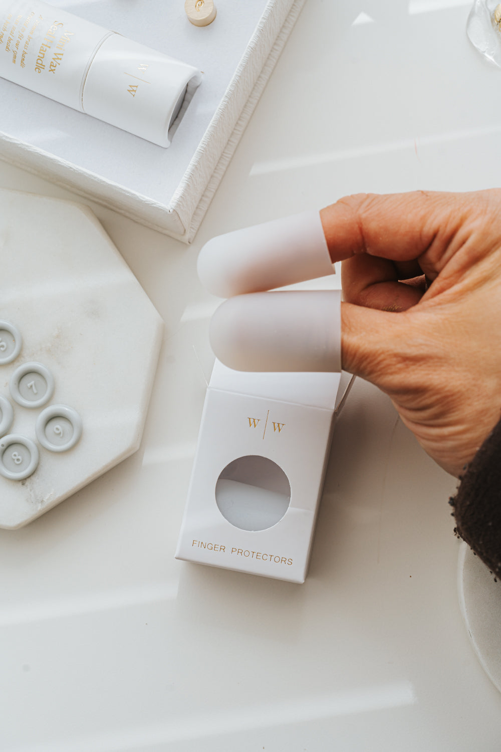 Hand wearing silicone finger protectors next to mini wax seal number set and packaging