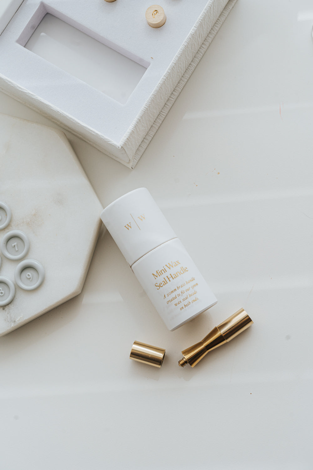 Mini wax seal handle with brass pieces and packaging beside numbered wax seals on marble surface